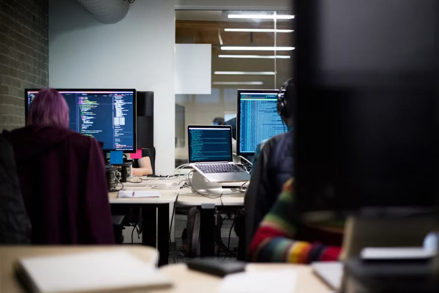 Engineers working at desks with code on their monitors